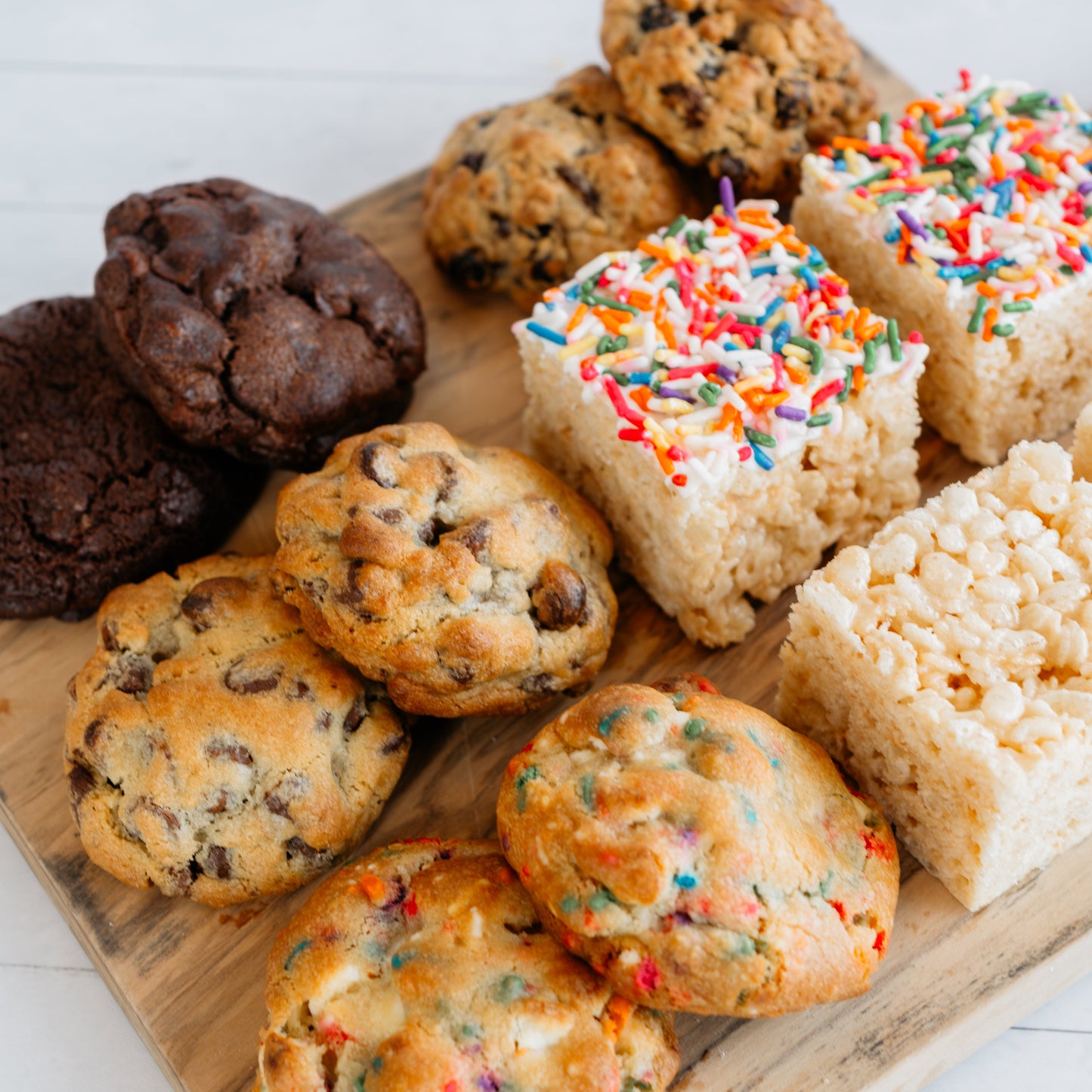 Assorted cookies including chocolate, oatmeal, and rice krispie treats on a wooden board.